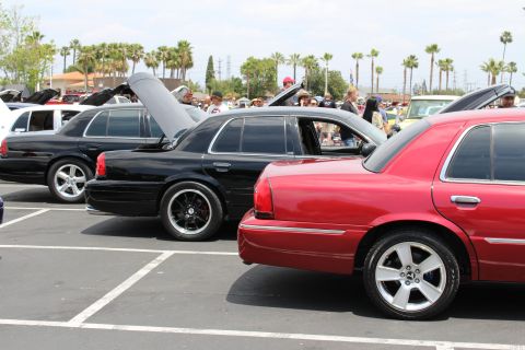Black and red full-size sedans with raised hoods at an outdoor car show