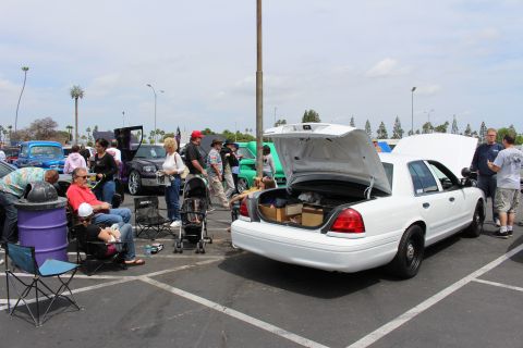 White Ford sedan with open trunk full of boxes at a car show