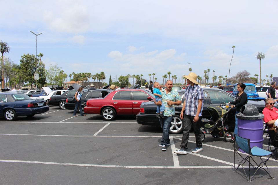 People walking through a parking lot of full-size sedans at a car show