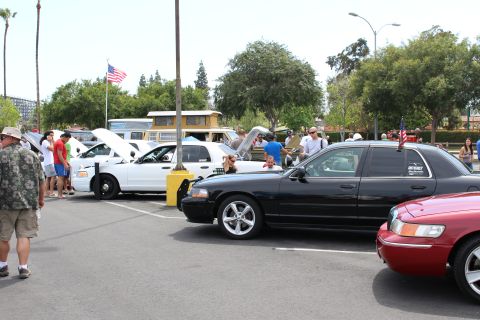 Black sedan parked beside a white police-style sedan and flag