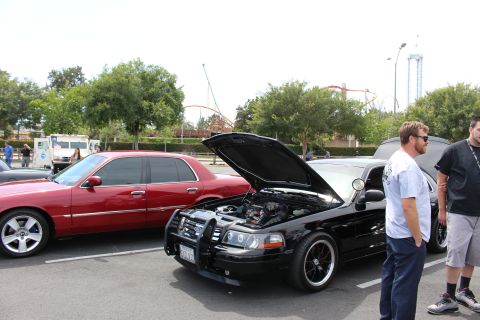 Black Ford sedan with open hood, men watching, coaster in background