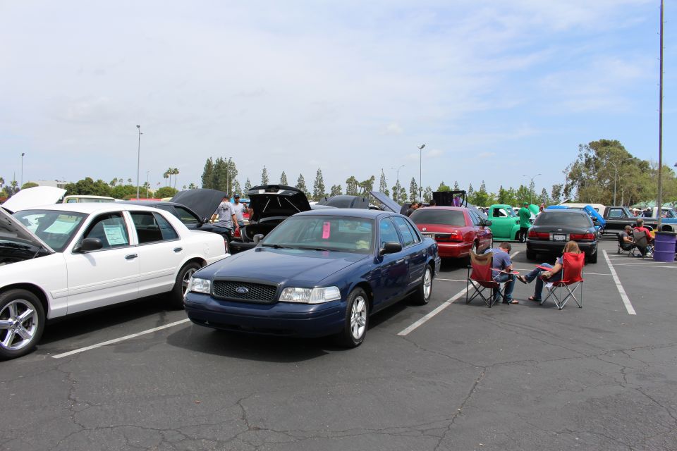 Dark blue Ford sedan parked in a lot with people in folding chairs nearby