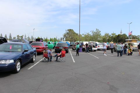 Wide view of a parking lot car show with cars, spectators, and an American flag