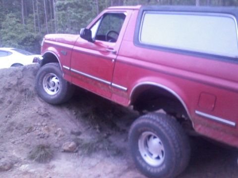 1992 Ford Bronco - This red 1992 Ford Bronco is shown navigating a steep dirt incline, with another vehicle visible behind it.