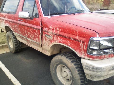 1992 Ford Bronco - Mud-splattered 1992 Ford Bronco parked on asphalt, showing its front passenger side.