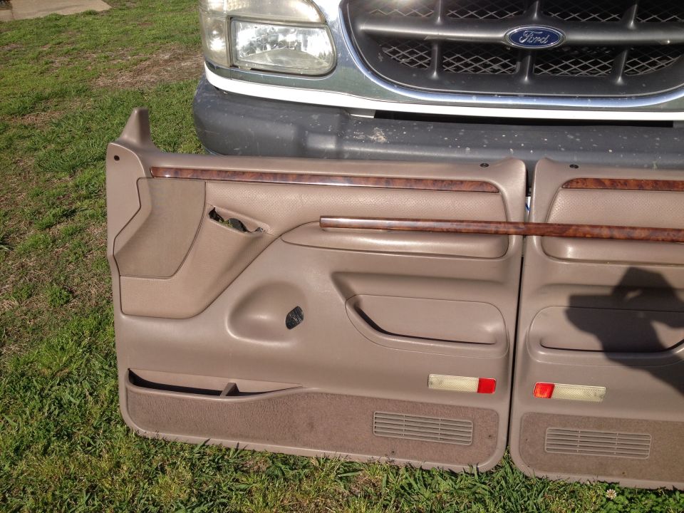 Two tan Ford door panels with wood trim, one damaged. A 1997 Ford Explorer grille is visible behind them