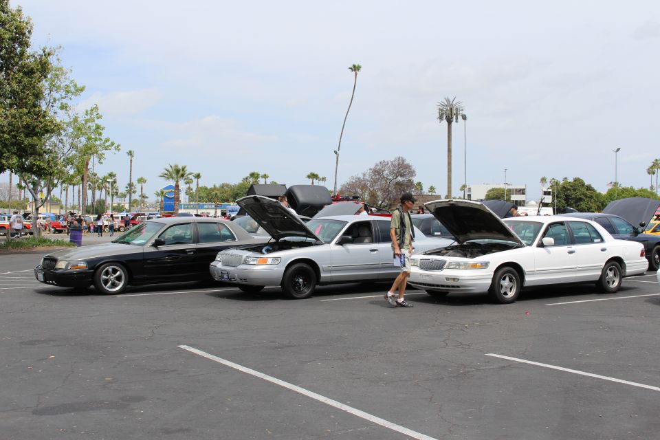Black, silver, and white full-size sedans with open hoods, a man walking between them