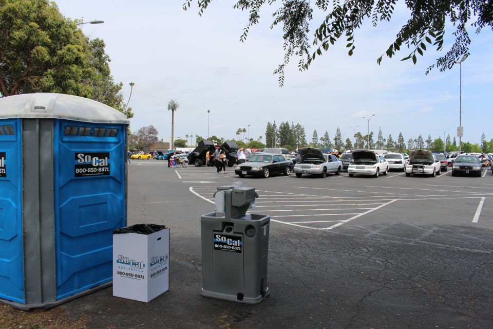 Blue SoCal portable toilet and gray hand-wash station overlooking a car show lot