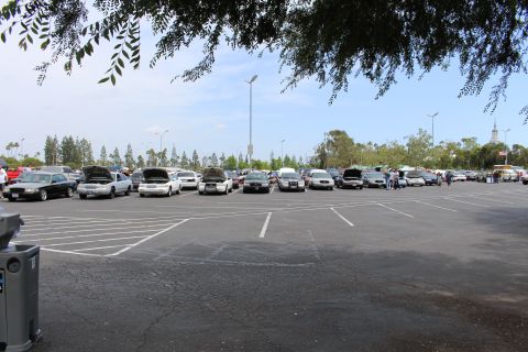 Wide distant view of a parking lot car show framed by overhanging tree branches