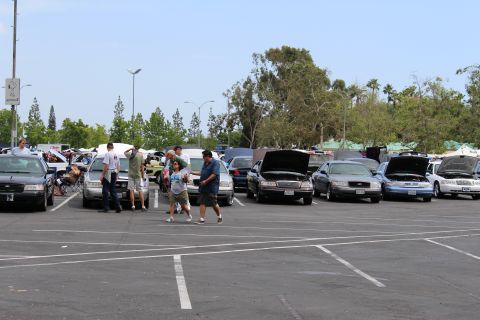 People walking among parked sedans with open hoods at a car show