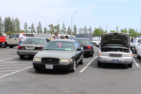 Black sedan with CA plate and silver sedan with open hood at a car show
