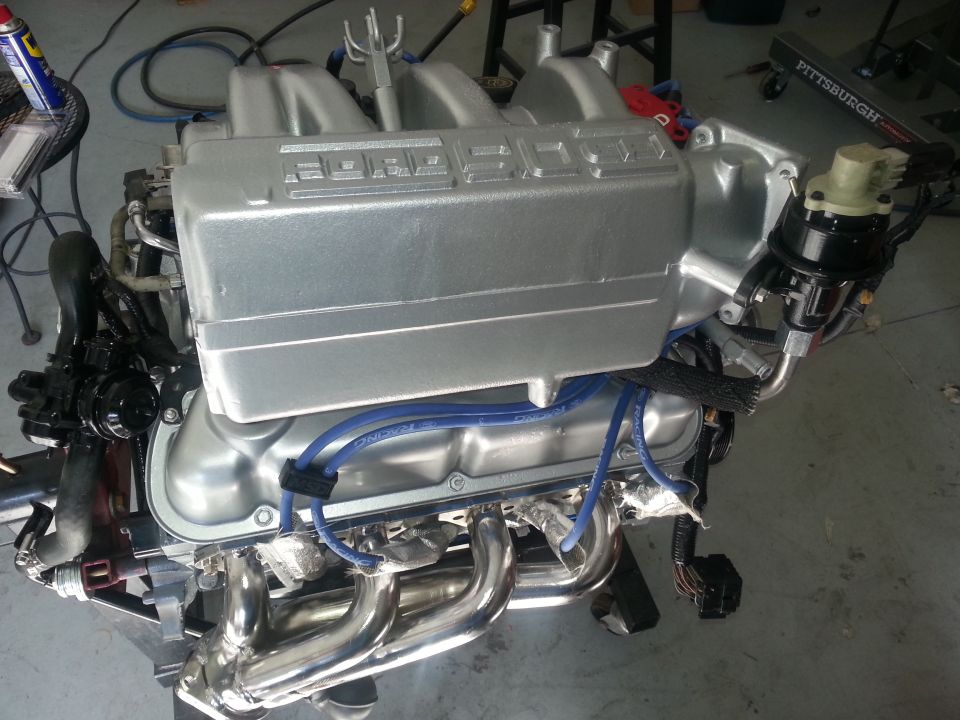 Silver Ford V8 engine with chrome headers and blue spark plug wires