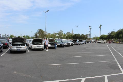 Row of sedans with hoods open along the edge of a vast parking lot