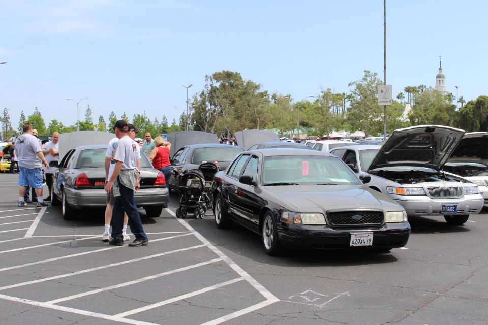 Black sedan with CA plate, wheelchair and people among show cars