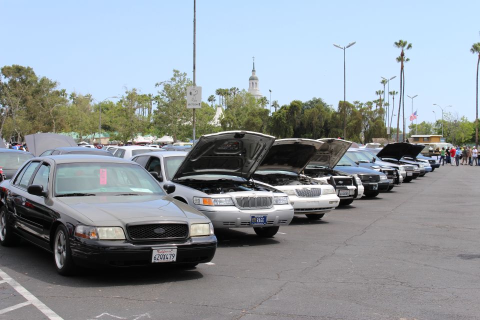 Black Ford sedan in foreground of a long row of cars with open hoods