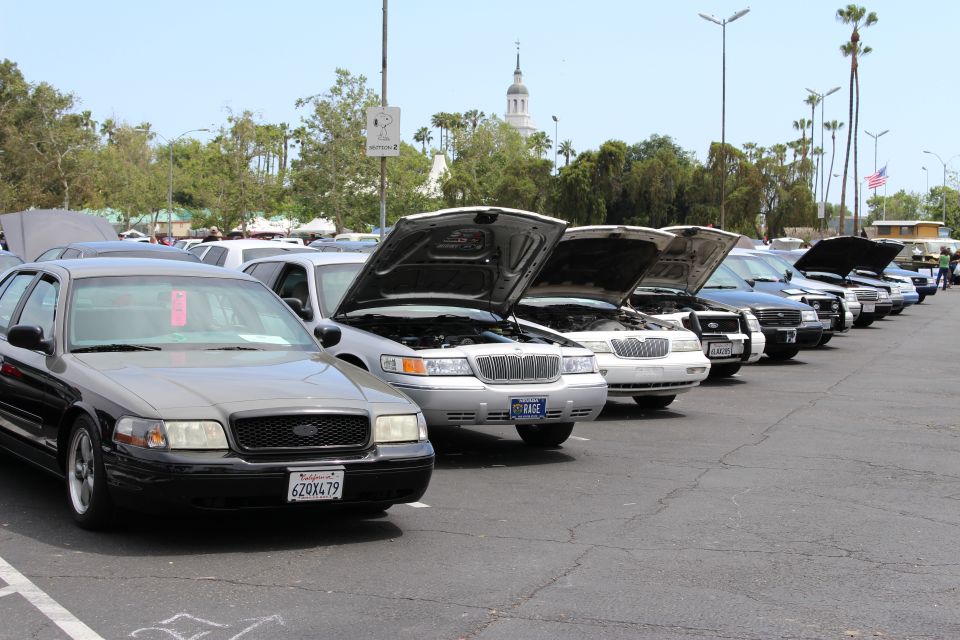Black sedan with CA plate heading a line of open-hood show cars