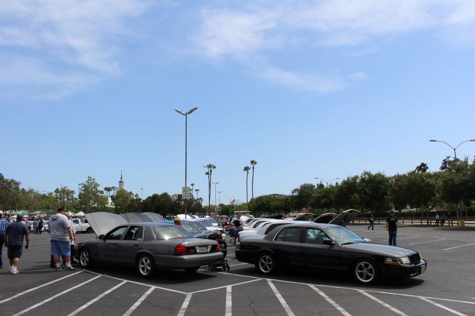 Gray and black sedans in foreground of a busy parking-lot car meet