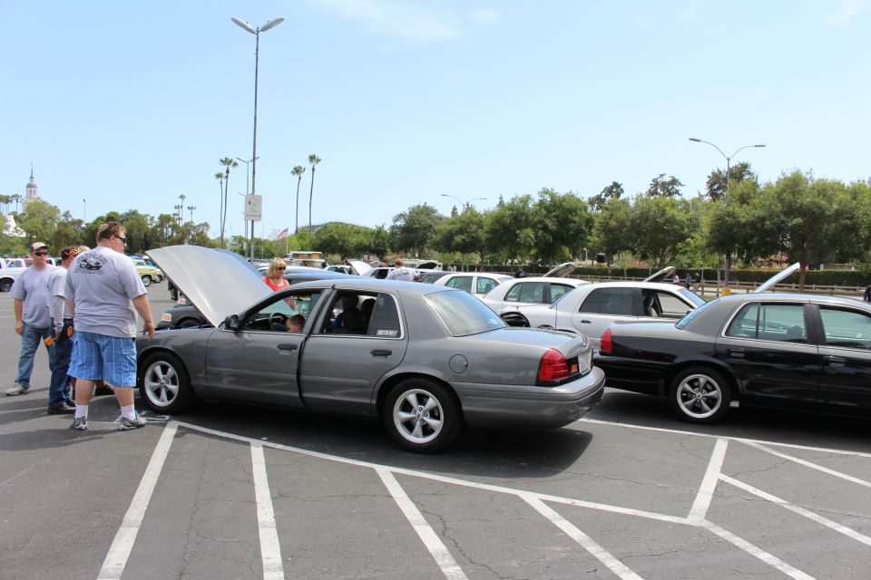 Gray sedan with hood up beside black sedan, spectators standing nearby