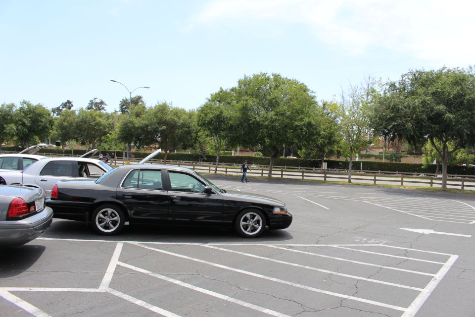 Black full-size sedan on chrome wheels parked in an empty lot with trees behind