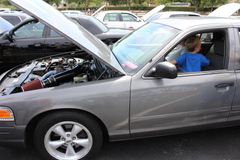 Engine bay of a gray sedan with a red cone air intake, a boy in the driver seat