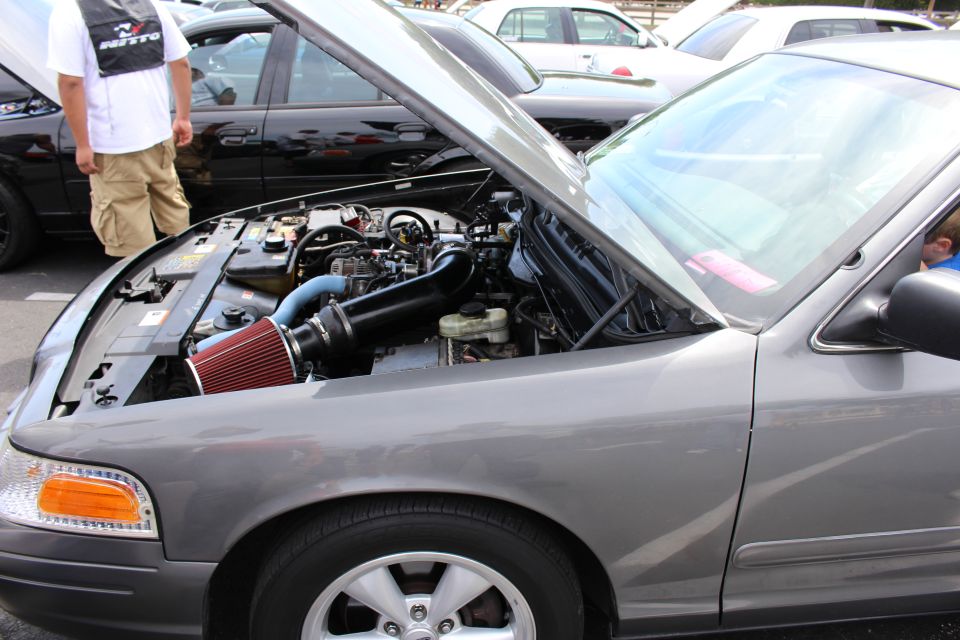 Engine bay of a gray sedan with red cone intake, a man standing nearby