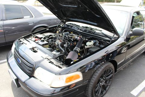 Black Ford sedan with hood up on black wheels showing engine and cone intake