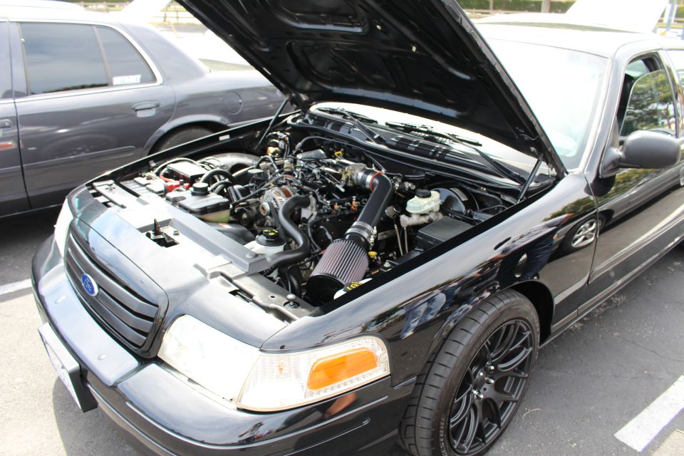 Black Ford sedan with hood up on black wheels showing engine and cone intake