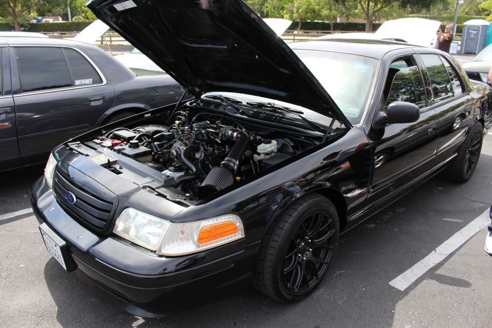 Black Ford sedan with raised hood and black wheels in a parking lot