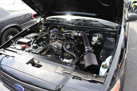 Engine bay of a black sedan with a black cone air intake and Ford grille badge