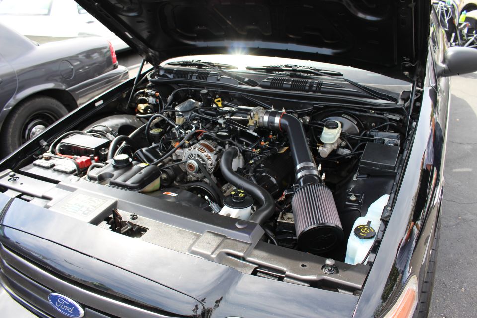 Engine bay of a black sedan with a black cone air intake and Ford grille badge