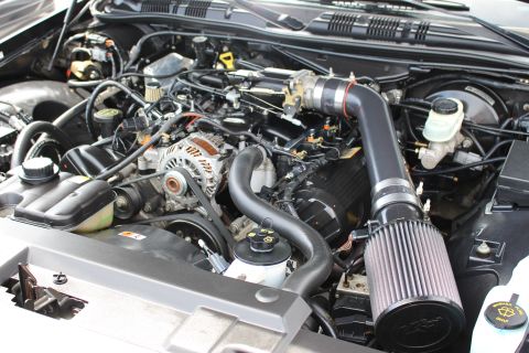 Close-up engine bay with black cone intake, master cylinder and wiring