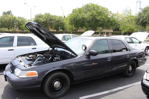 Dark gray sedan on black steel wheels, hood up, white sedans behind