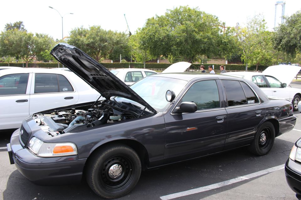 Dark gray sedan on black steel wheels, hood up, white sedans behind