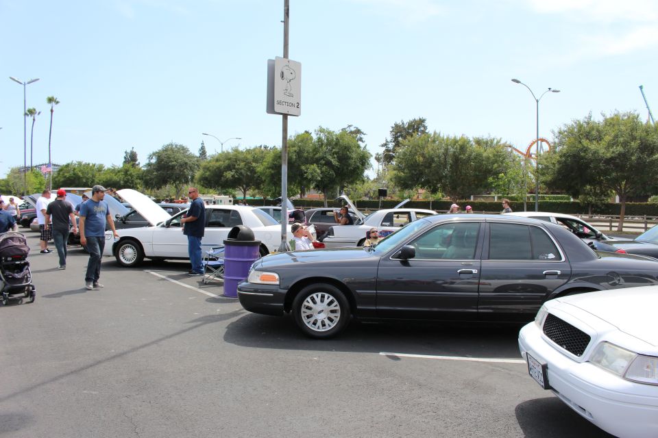 Row of full-size sedans at an outdoor car show with people walking the lot