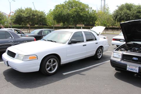 White Ford Crown Victoria parked next to a black Ford sedan with hood open