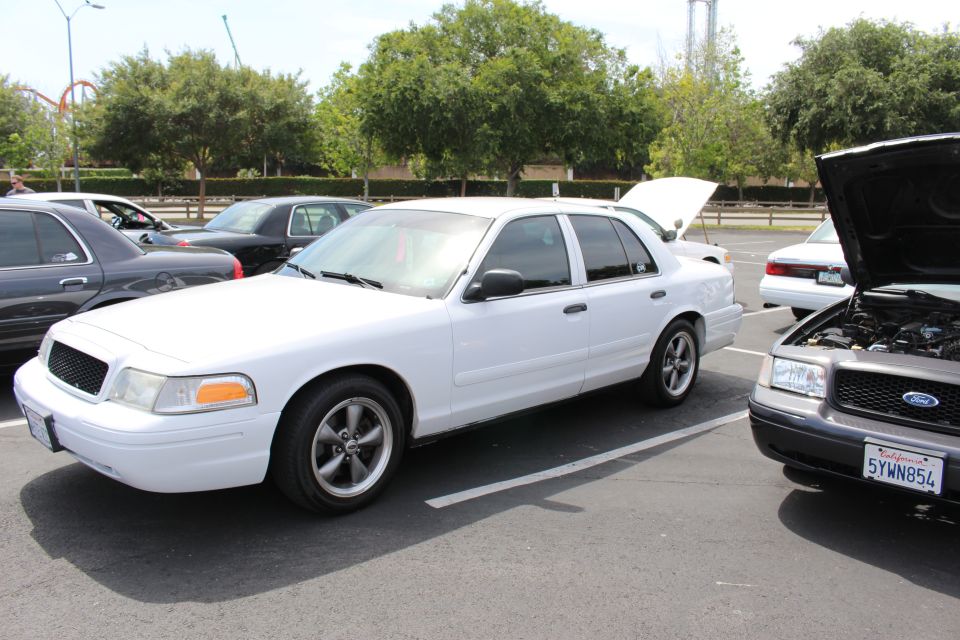 White Ford Crown Victoria parked next to a black Ford sedan with hood open