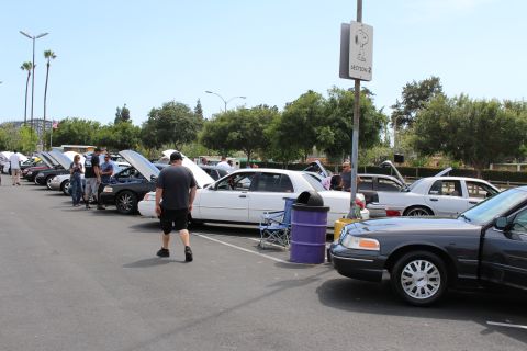 People and full-size sedans with raised hoods at an outdoor car meet