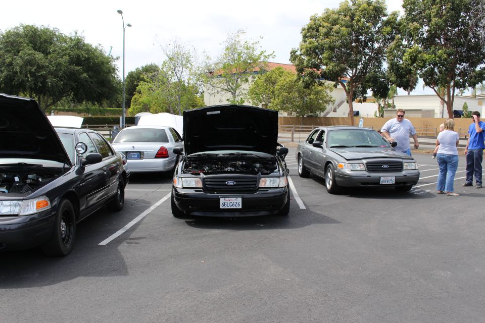 Three dark Ford Crown Victoria sedans, center one with hood open, in a lot