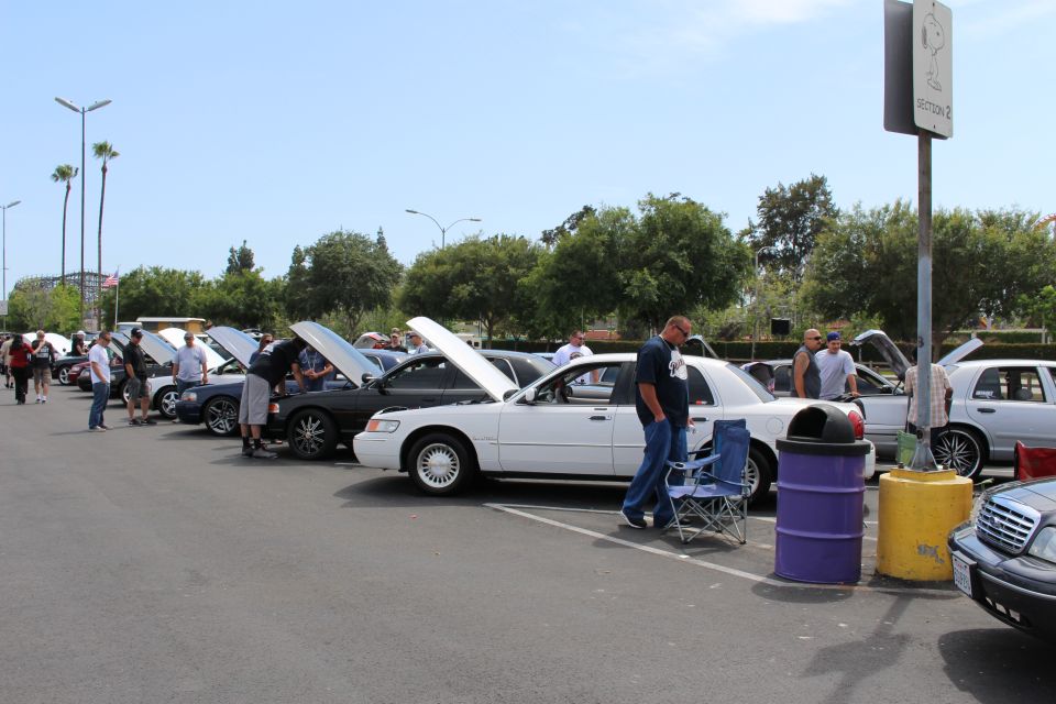 White and dark full-size sedans with hoods open and people at a car meet