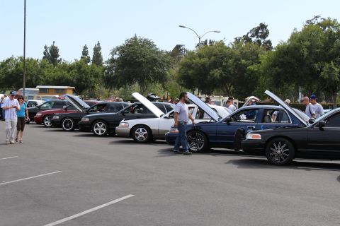 Long row of sedans with hoods open and spectators at a car show
