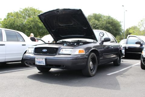 Dark gray Ford Crown Victoria with raised hood among parked cars