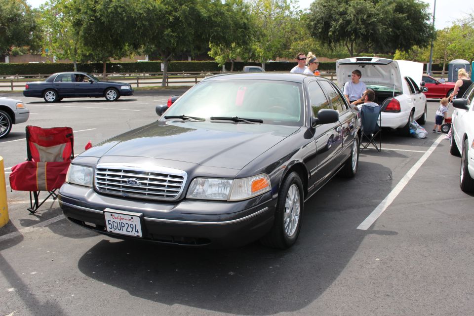 Dark gray Ford Crown Victoria parked with camp chairs and people behind
