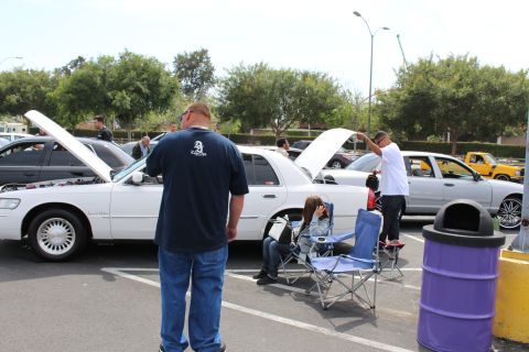 Man standing beside a white Mercury sedan with open hood at a car meet