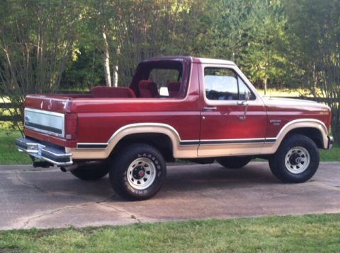 1986 Ford Bronco - This 1986 Ford Bronco features a two-tone red and tan paint scheme and is shown from a 3/4 front angle.