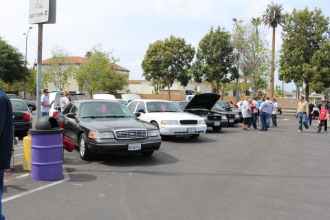 Row of black and white full-size sedans parked along a lot with people