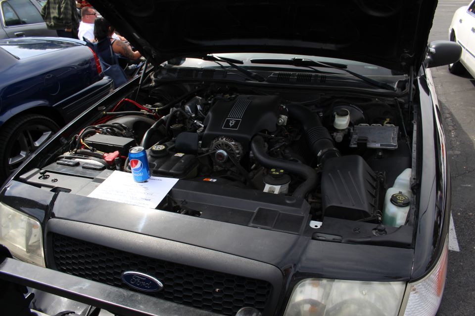 Engine bay of a black Ford sedan with hood open at a car show