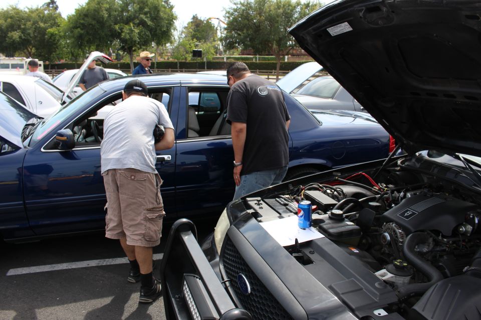 Two men inspecting a blue sedan with open hood at a car show