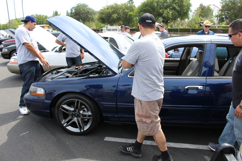 Man closing the hood of a blue sedan at a car show