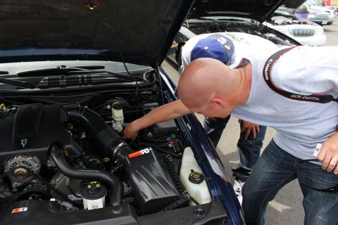 Man inspecting engine bay of a blue sedan with K&N filter