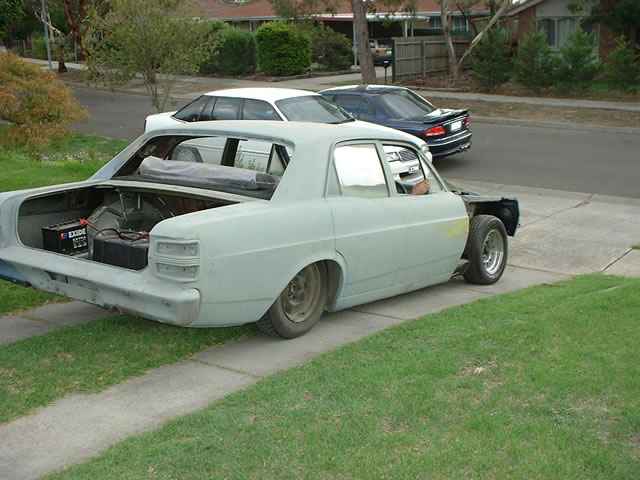 Gray primer project sedan with open trunk and relocated battery on a suburban driveway